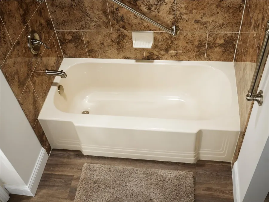 New bathtub with stone-look wall surround and grab bar